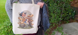 A natural cotton tote bag featuring a Renn Faire or fantasy inspired girl running through oversized mushrooms. She wears a kerchief and a plaid skirt, and her hair is floating behind her.